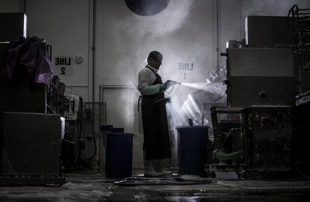 Man wearing protective clothing spraying industrial equipment clean, 在黑暗和充满蒸汽的环境中